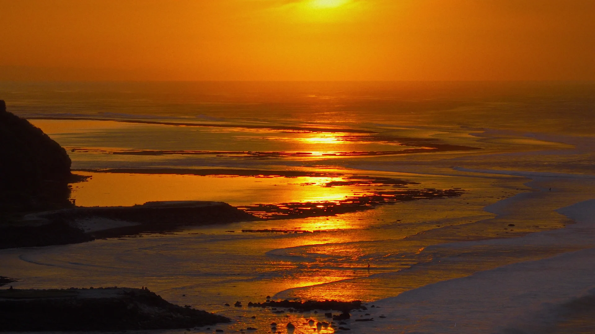 An orange sunset reflected in the moving surf at Uluwatu.